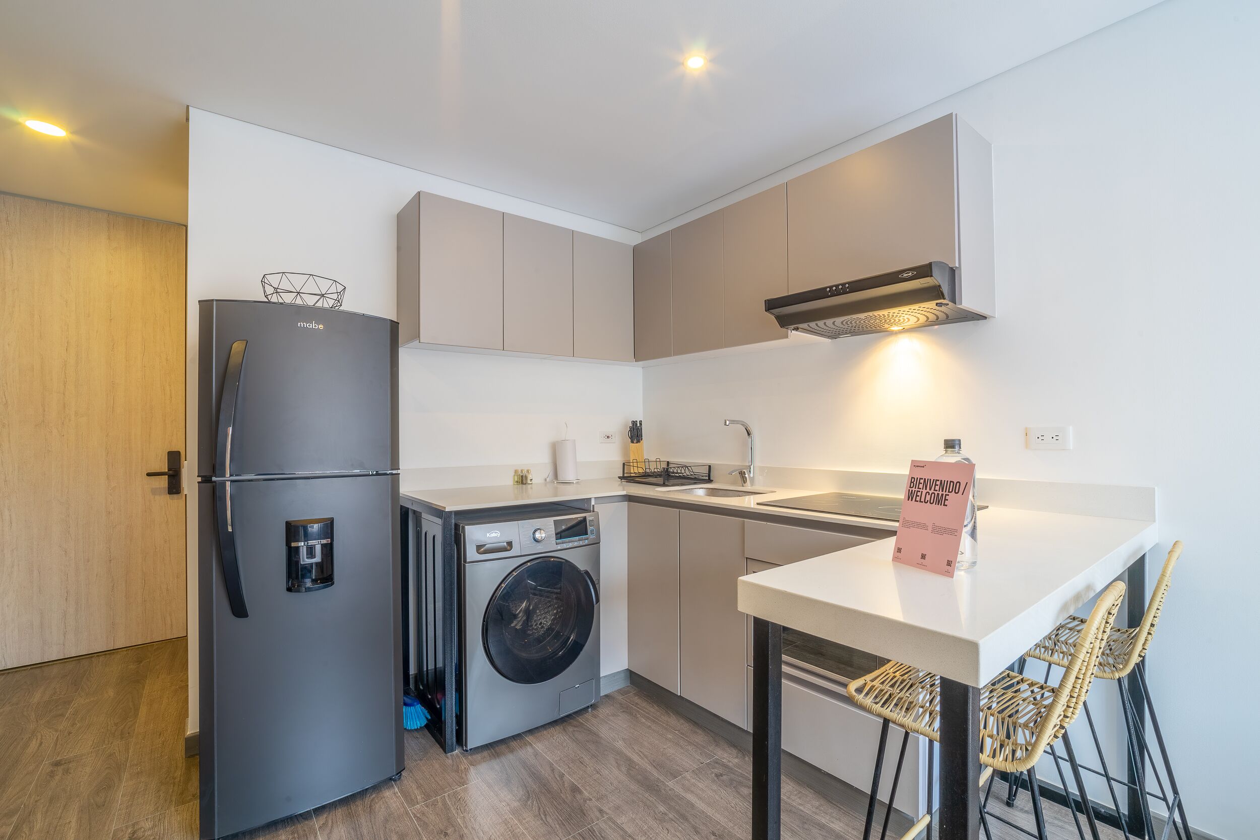A compact kitchen with a built-in washing machine, a refrigerator, and a dining area with a table and chairs.
