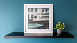 A framed picture of a train on tracks, placed on a black shelf against a teal wall.