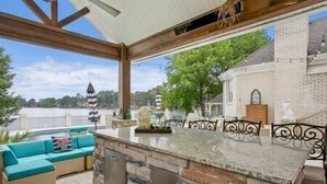 An outdoor kitchen area with a stone countertop and metal cabinets, a blue sofa, and a view of a lake and buildings in the background.