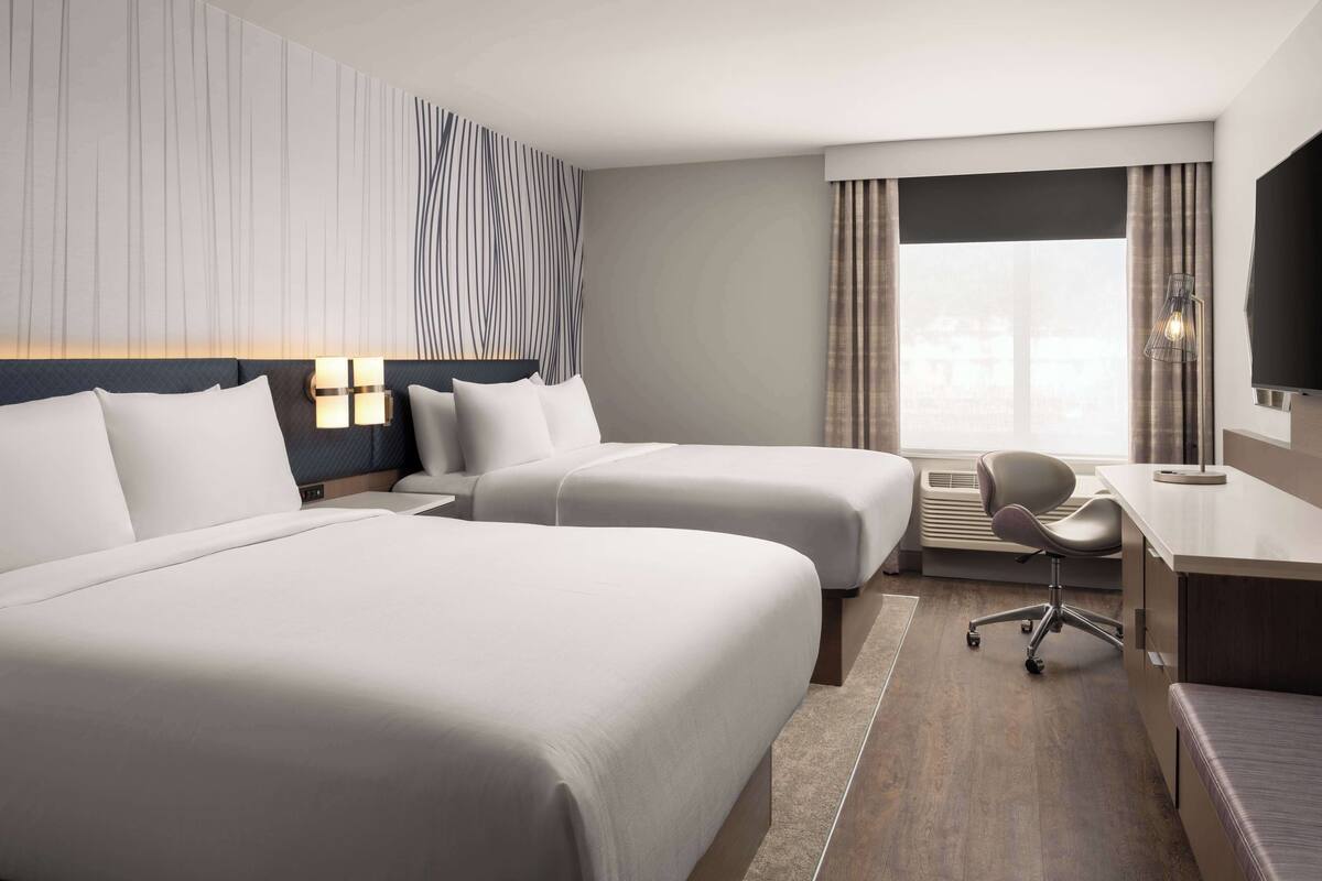 Een hotelkamer met twee bedden, een bureau, een stoel en een groot raam met gordijnen.