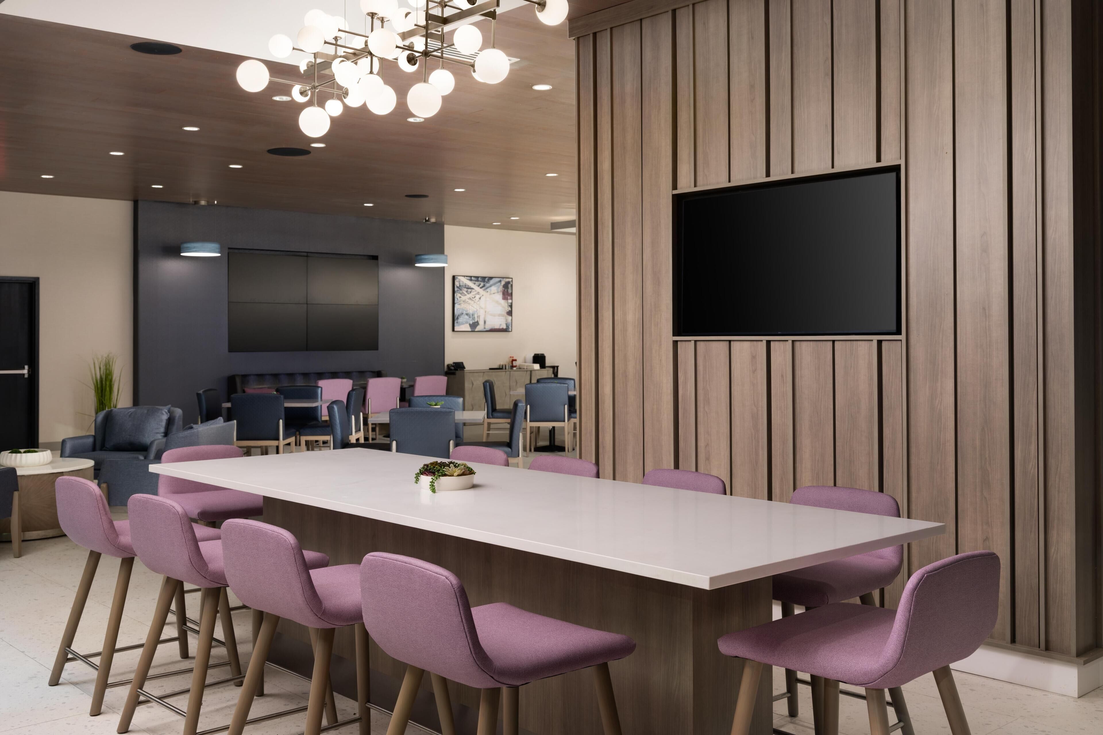 A modern meeting room with a large table, purple chairs, a flat-screen TV, and wooden paneling.
