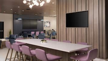 A modern meeting room with a large table, purple chairs, a flat-screen TV, and wooden paneling.