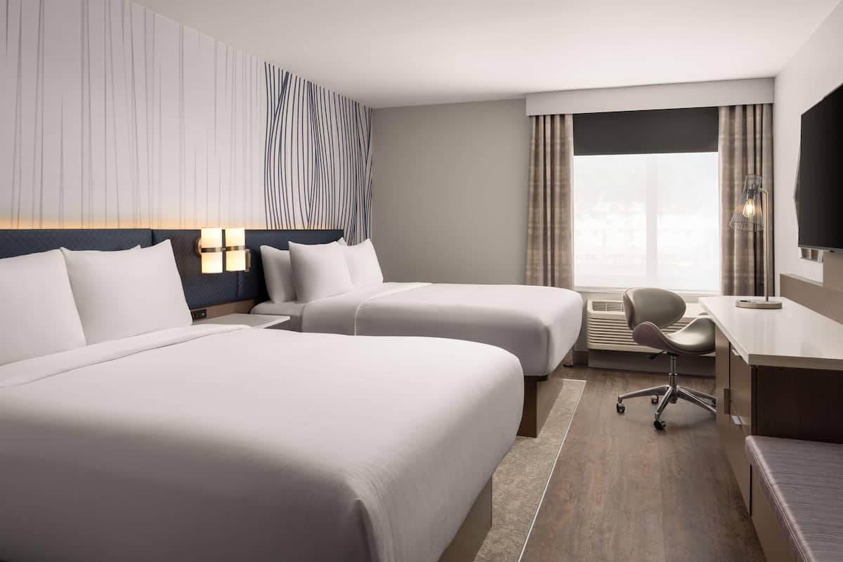 Een hotelkamer met twee bedden, een bureau, een stoel en een groot raam met gordijnen.