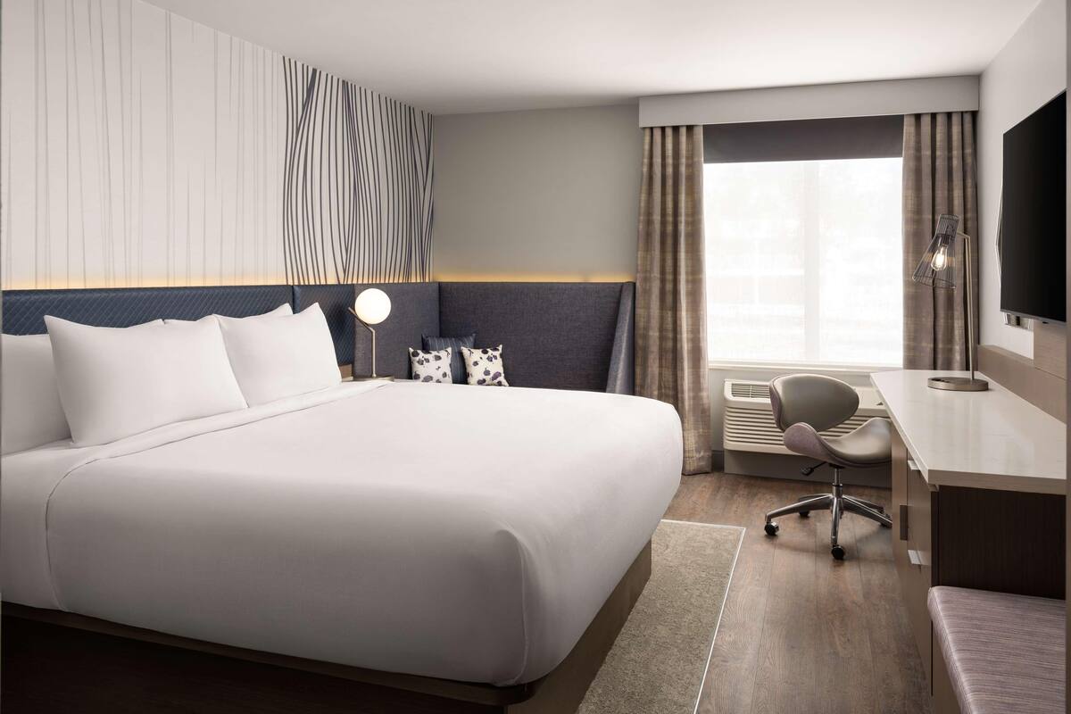 Hotelkamer met een groot bed, een bureau, een stoel, een flatscreen televisie en een raam met gordijnen.