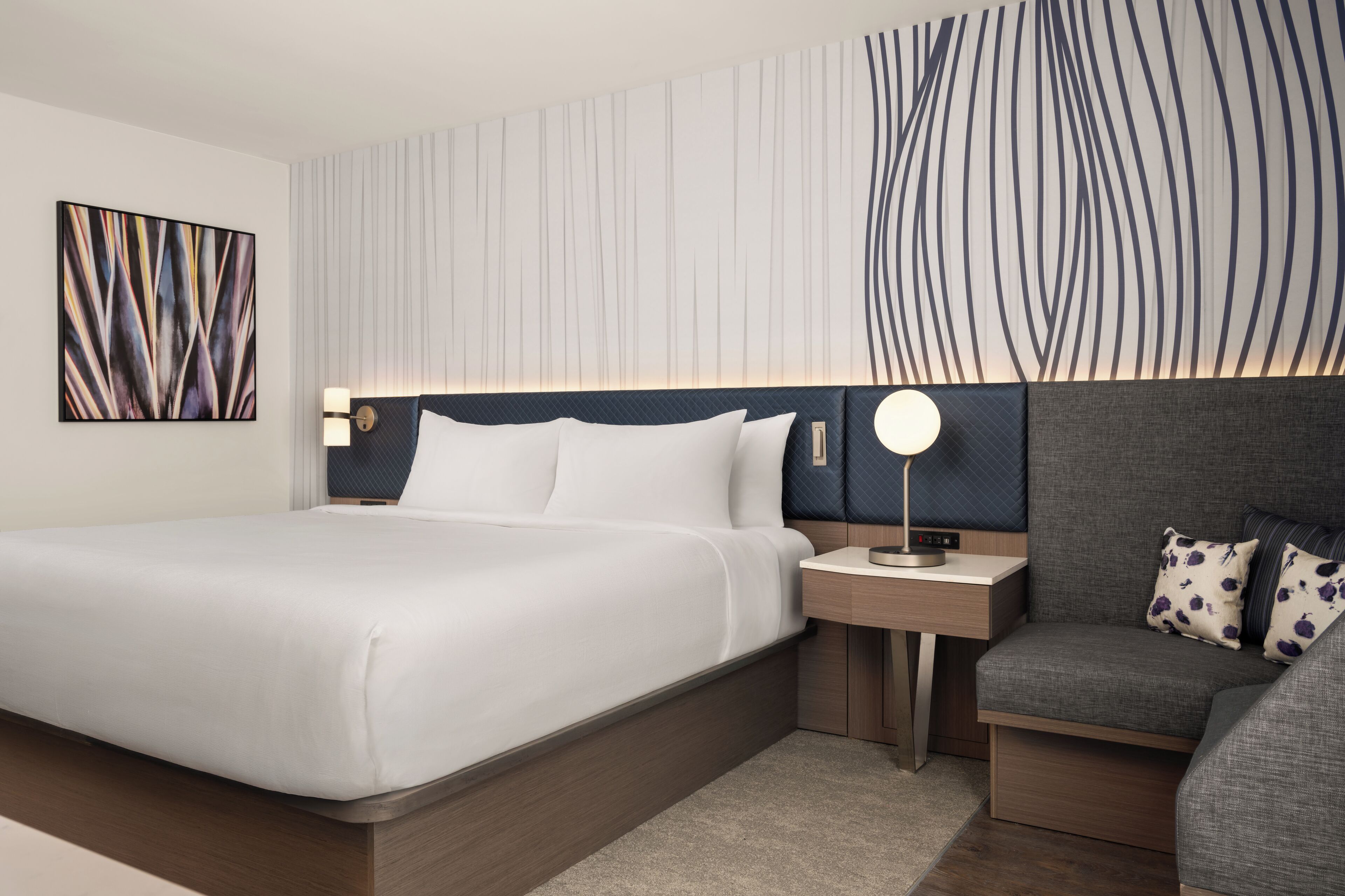 A modern hotel room with a large bed, bedside tables, a desk, and a sofa.