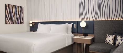 A modern hotel room with a large bed, bedside tables, a desk, and a sofa.