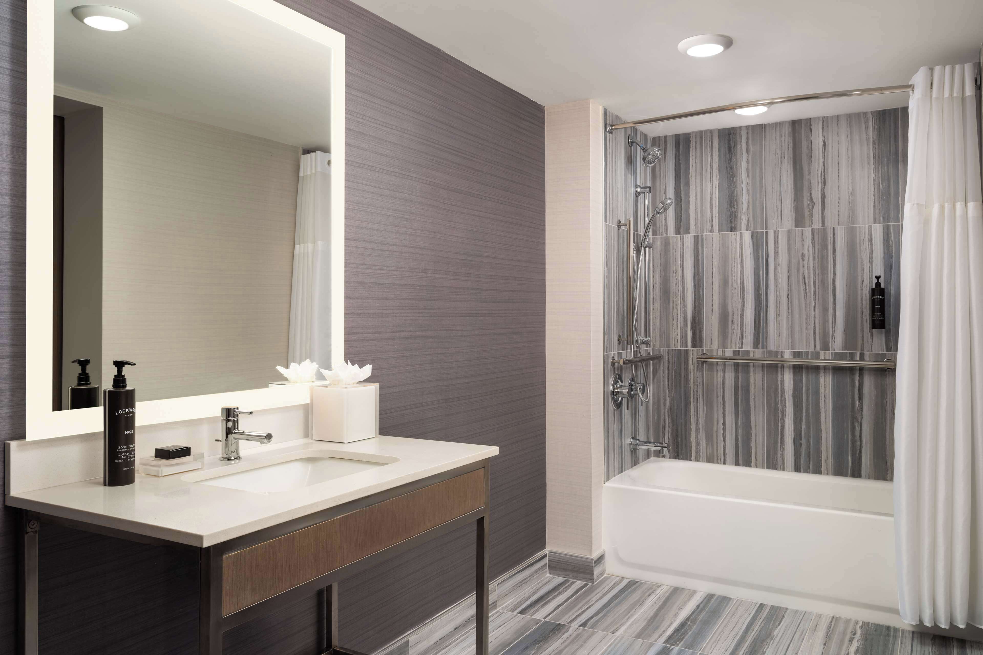 A modern bathroom with a large mirror, a white sink, a vanity, and a shower with a glass door.