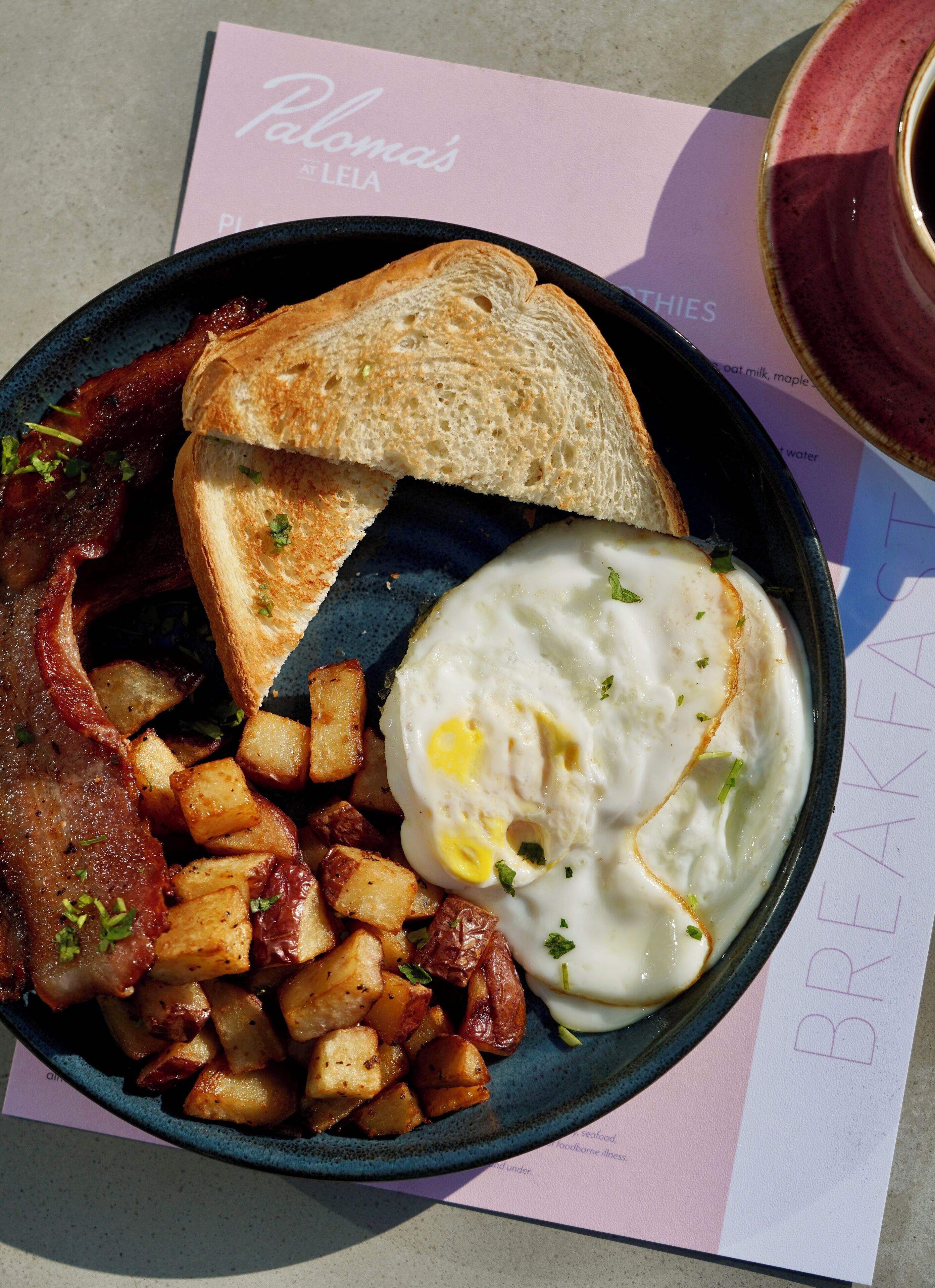 Un plato de desayuno con tostadas, tocino, huevos y papas.
