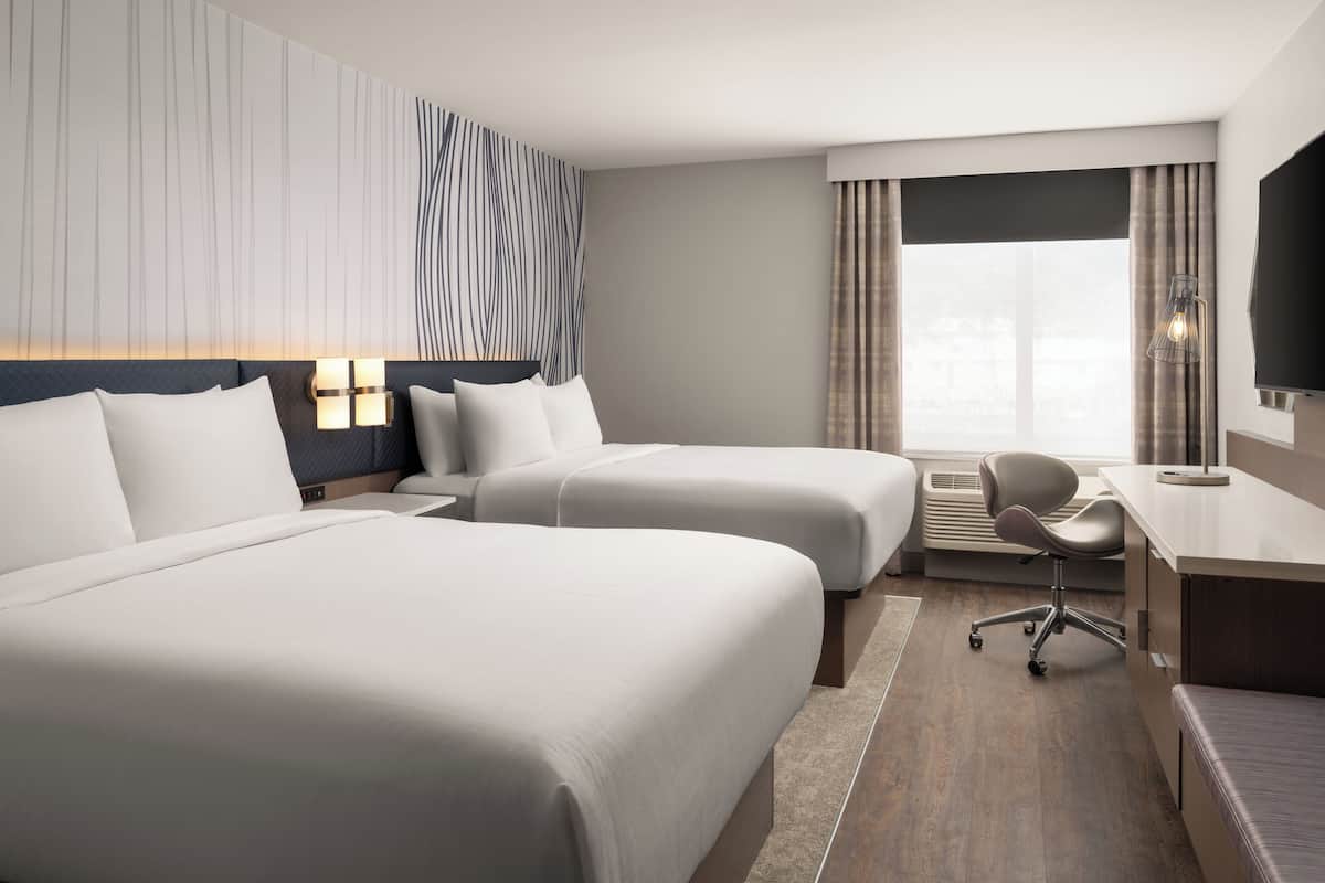 Een hotelkamer met twee bedden, een bureau, een stoel en een groot raam met gordijnen.