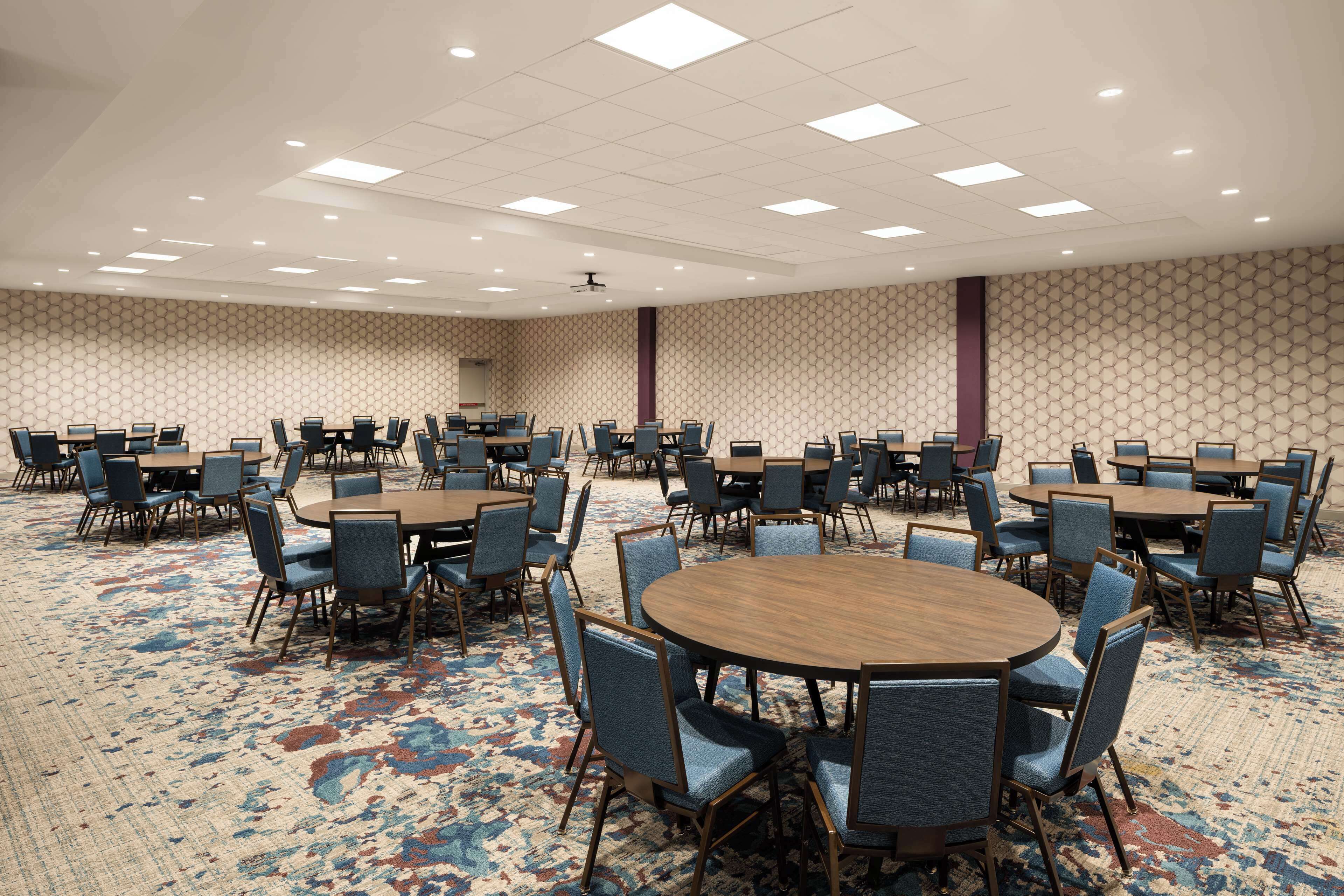 A large conference room with multiple round tables and chairs, carpeted floor, and a patterned wall.