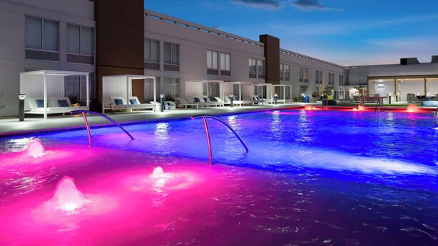 Een modern hotel met een zwembad, comfortabele loungeruimtes en een goed verlichte gevel.
