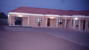 A building with a red-tiled roof, multiple doors, and potted plants. - Ikhutse Guest House (Kanye)