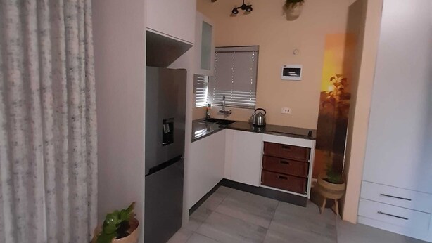 A compact kitchen with a refrigerator, a sink, and a window with blinds. - Ikhutse Guest House (Kanye)