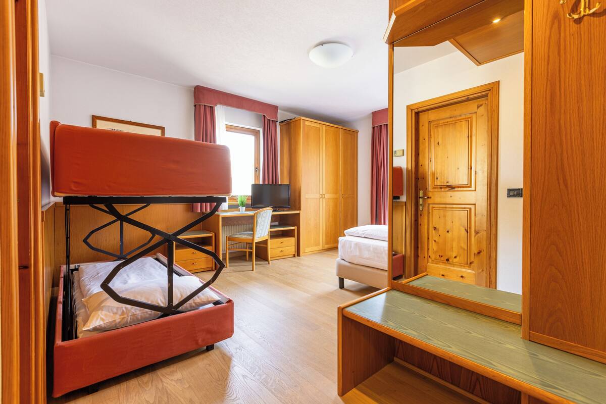 A compact bedroom with a bunk bed, a desk with a chair, a bed, and a wardrobe.