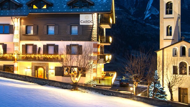 Un hotel con un cartel que dice "CARDO HOTEL" frente a una montaña cubierta de nieve.