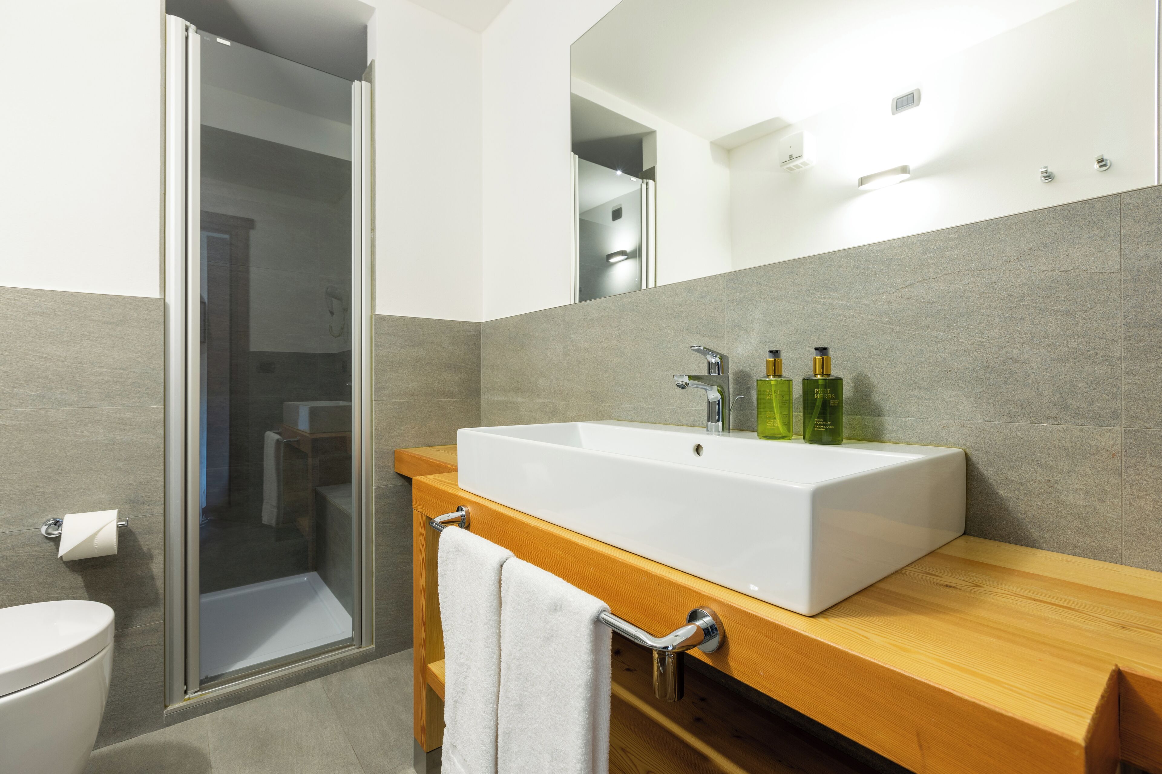 A modern bathroom with a large white sink, a glass shower enclosure, and a wooden vanity.