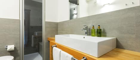 A modern bathroom with a large white sink, a glass shower enclosure, and a wooden vanity.