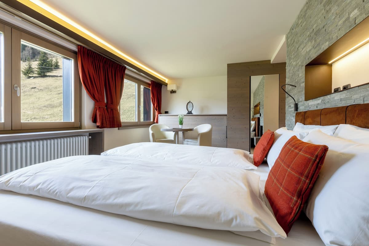 A hotel room with a large bed, a dining area, and a view of the outdoors.