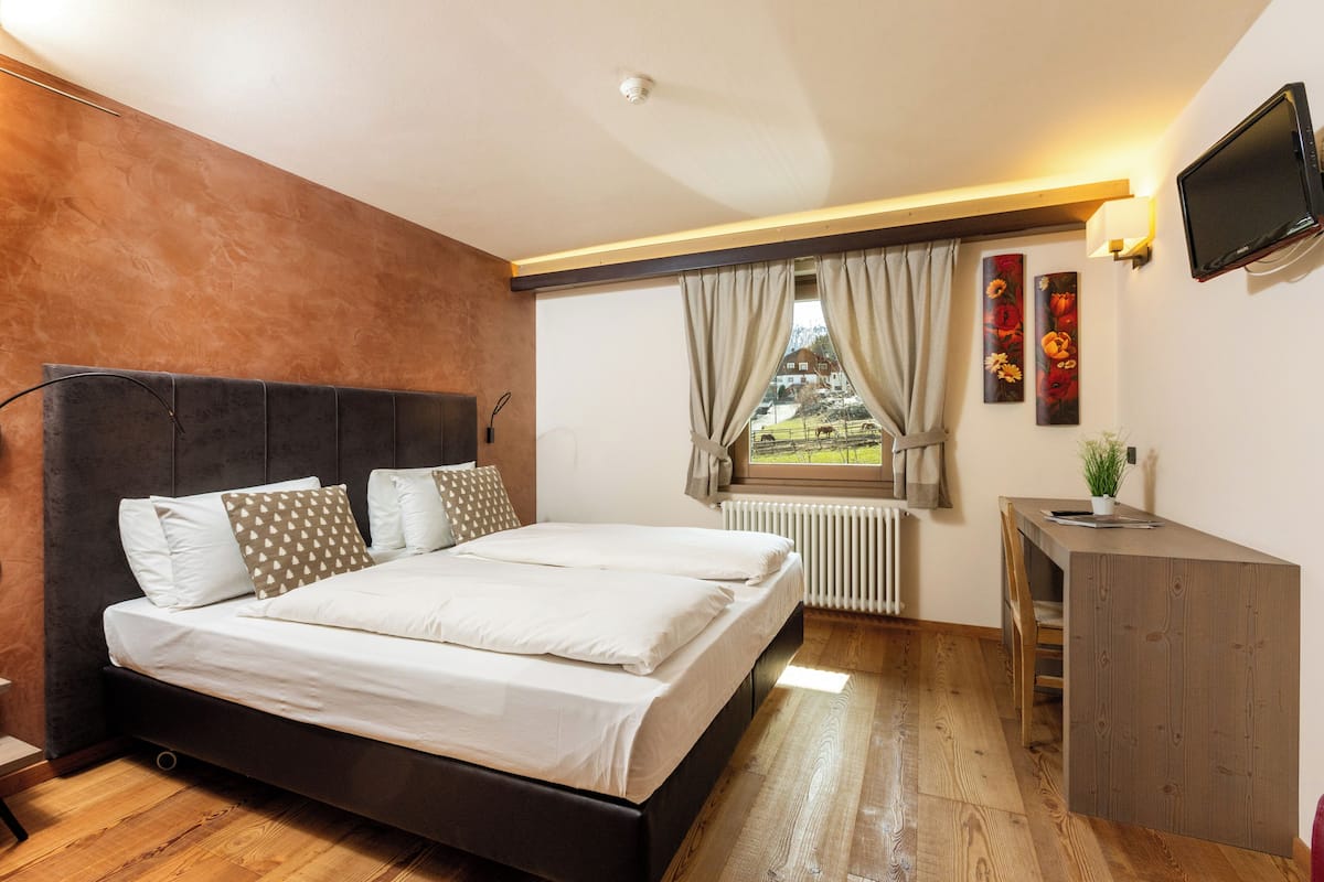 A modern bedroom with a large bed, a desk, and a TV.