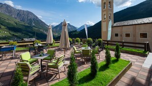 Un patio al aire libre con mesas y sillas, una mesa de billar y vistas a montañas y una torre de iglesia.