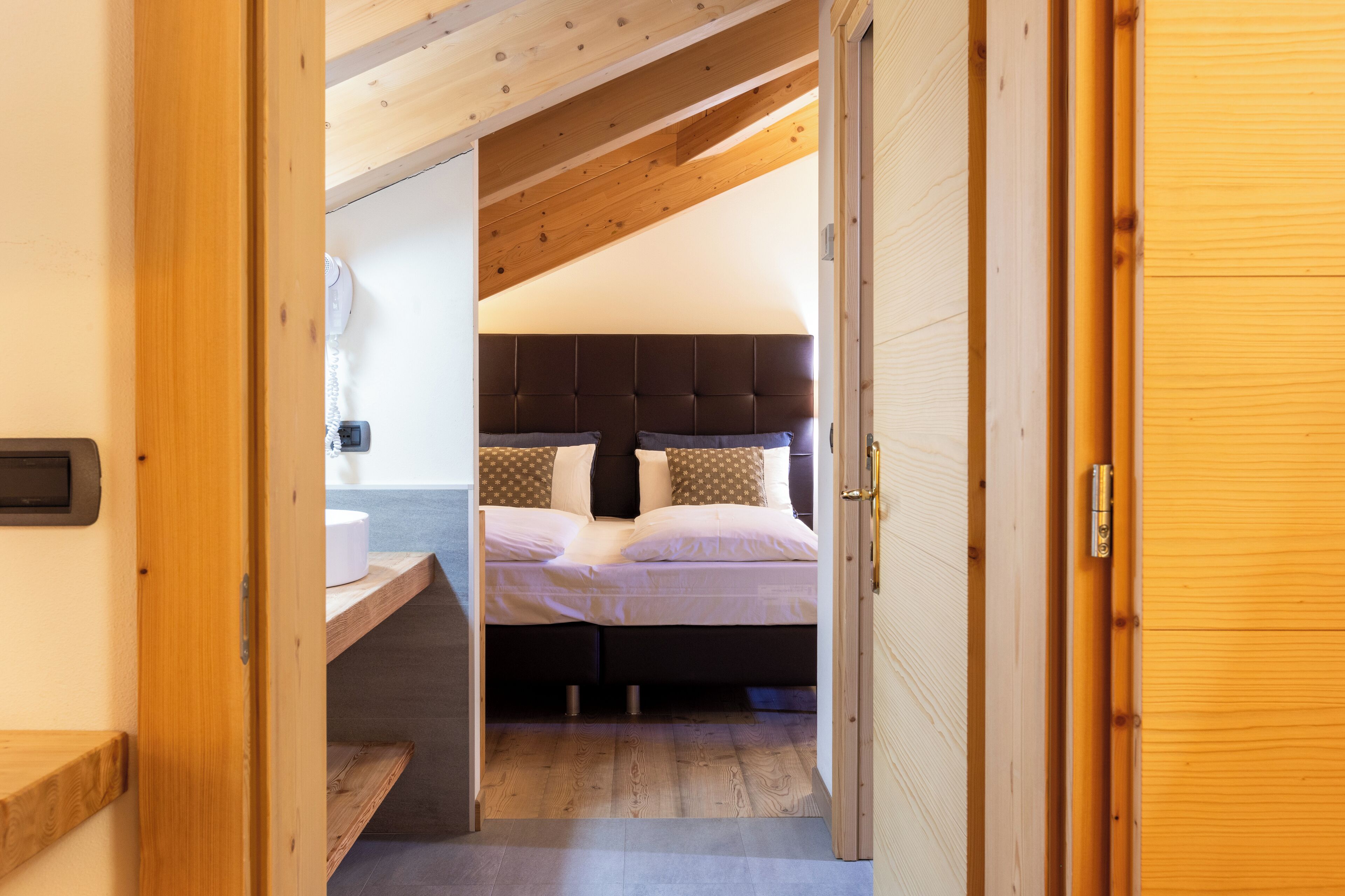 Un dormitorio con techo de madera, una cama con muchos almohadones y una mesita de noche pequeña.