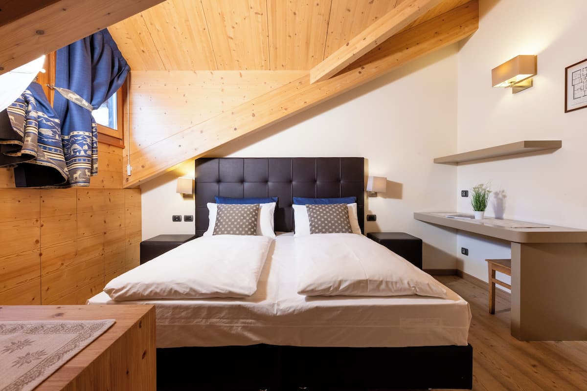 A bedroom with a bed, bedside tables, a desk, and a window with curtains.