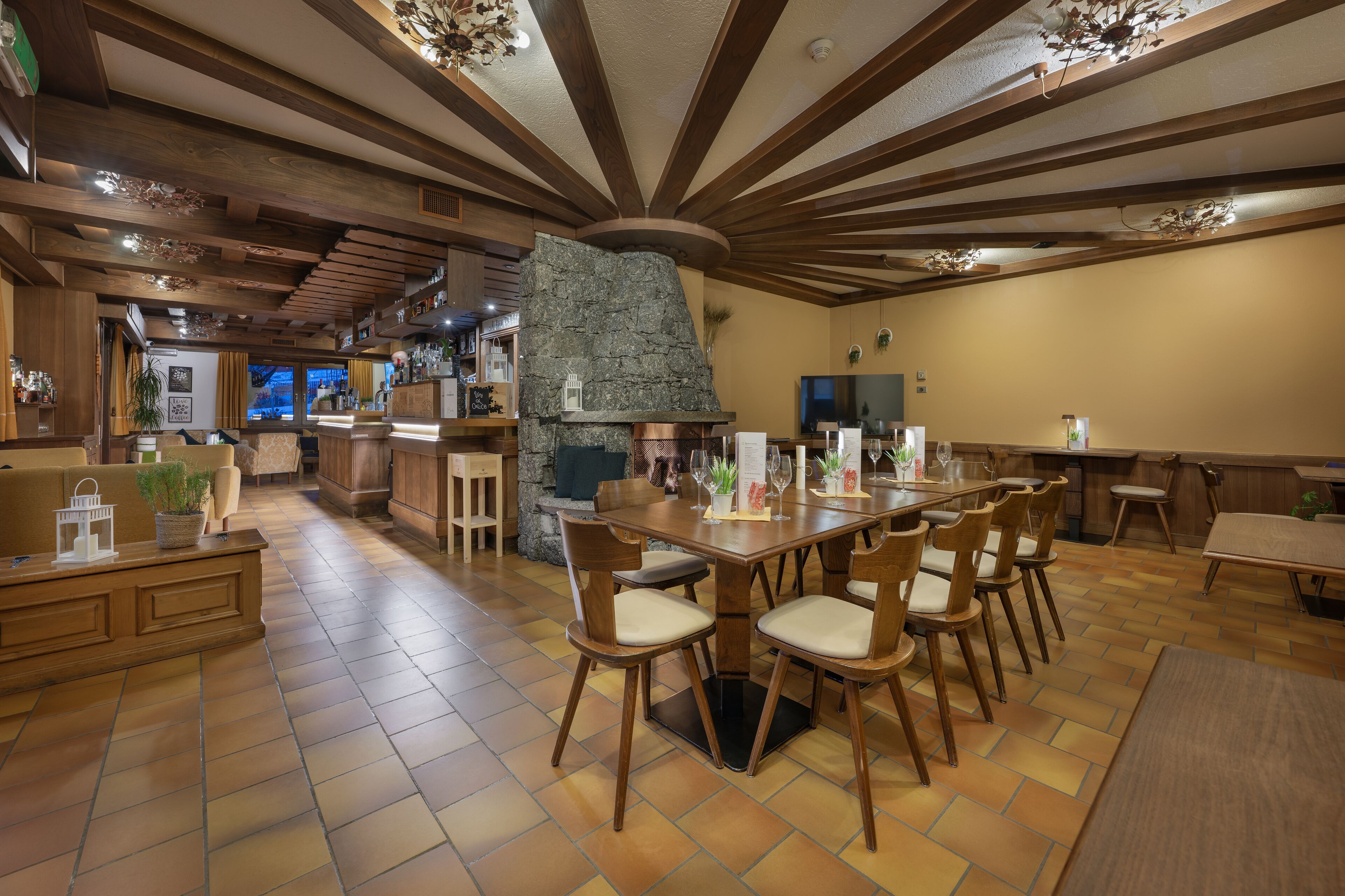 A spacious dining area with a stone fireplace, wooden ceiling beams, and a large table with chairs.
