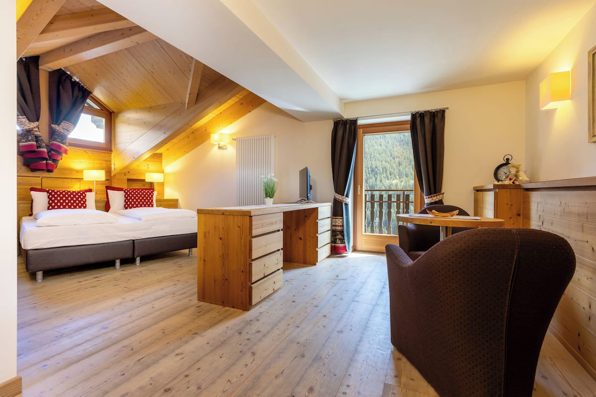 A cozy room with a wooden ceiling, a bed with red and white polka dot pillows, a desk with drawers, and a chair.
