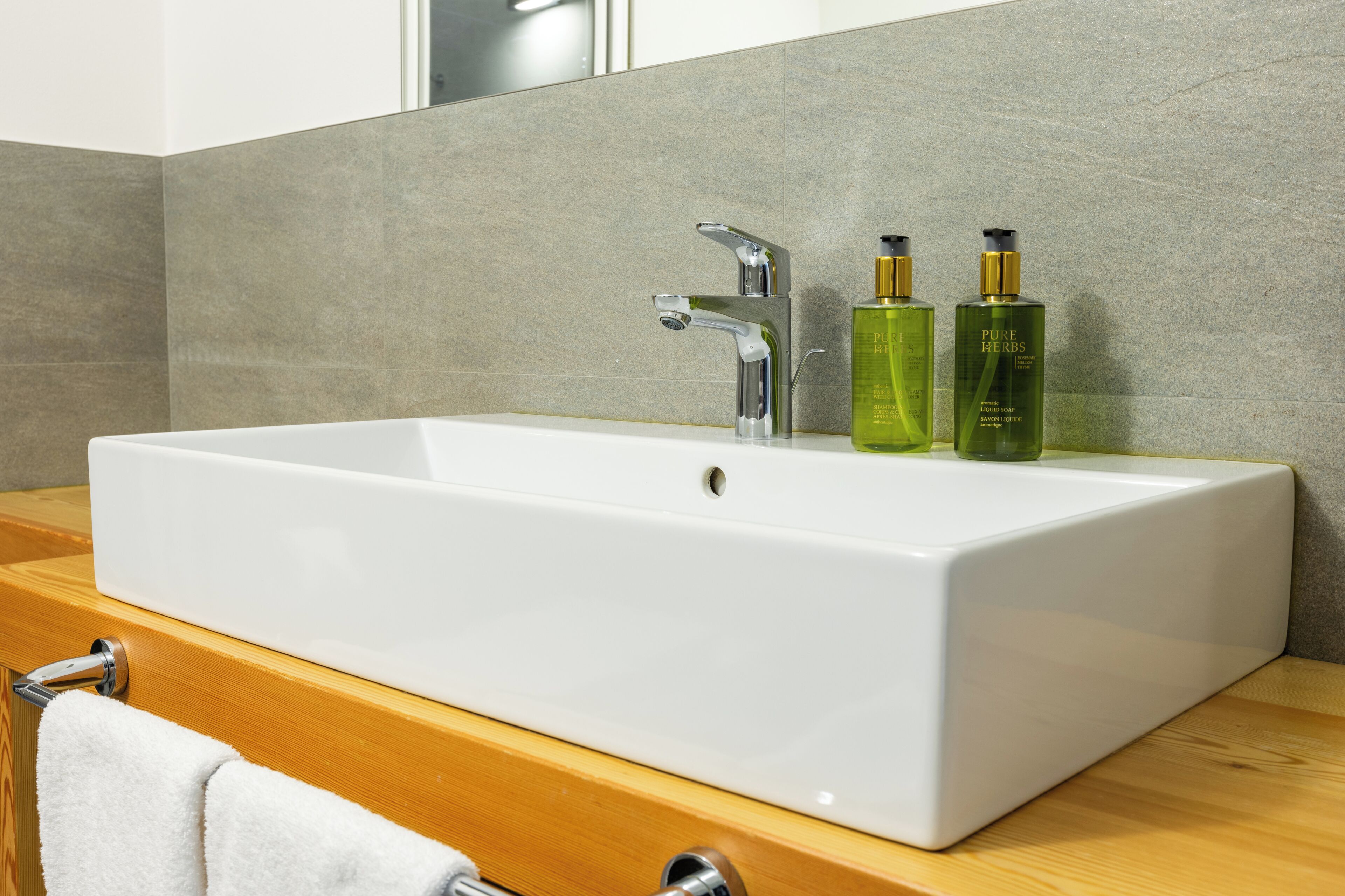 A modern bathroom with a rectangular white sink, a chrome faucet, and two green bottles of Pure Herbs on the countertop.