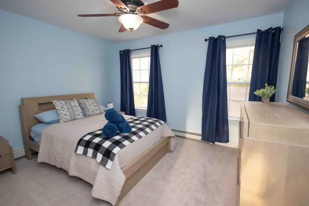 A bedroom with a bed, a ceiling fan, a dresser, and a window with curtains.