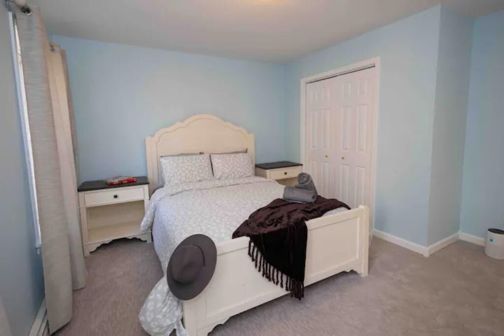 A bedroom with a white bed, a nightstand, a dresser, and a door.