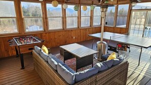A wooden deck with a foosball table, a sofa with cushions, a table, and a hanging lamp. - Spacious 5 BR w/Mountaintop Views-2 Min to Hunter (Tannersville)