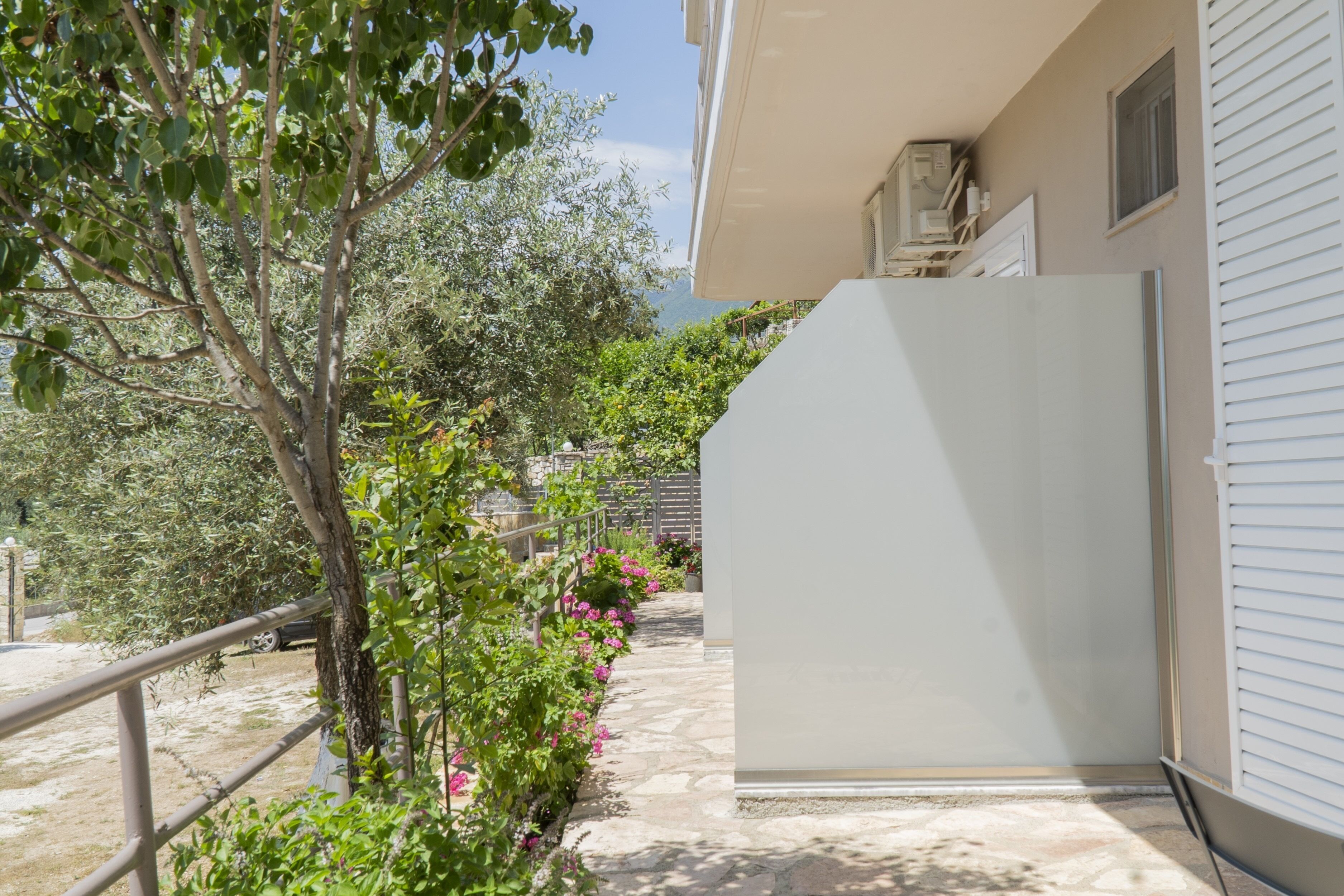 Un balcone con un vialetto in pietra, un albero e un edificio dalla facciata bianca.