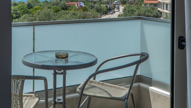 A balcony with a glass table and two wicker chairs, overlooking a coastal town with buildings and a mountain in the distance. - Koks’ Guesthouse  (Himarë)
