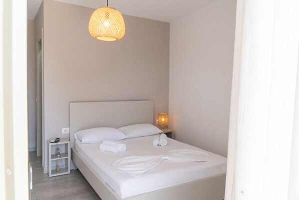 A neatly made bed with white linens, a bedside lamp, and a small nightstand with a phone and a bottle.
