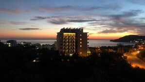 A high-rise hotel with multiple floors, surrounded by trees and a view of the sea at sunset. - Koks’ Guesthouse  (Himarë)