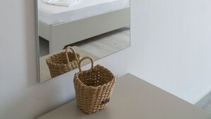 A modern hotel room with a large mirror, a bed with white linens, a hanging light fixture, and a small table with a woven basket. - Koks’ Guesthouse  (Himarë)