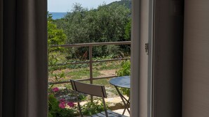 An open door leading to a balcony with a table and chairs, overlooking a garden and a distant view of the sea. - Koks’ Guesthouse  (Himarë)