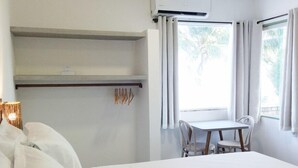 Camera d'albergo con un letto grande, un tavolino, sedie, un climatizzatore e una finestra con tende.