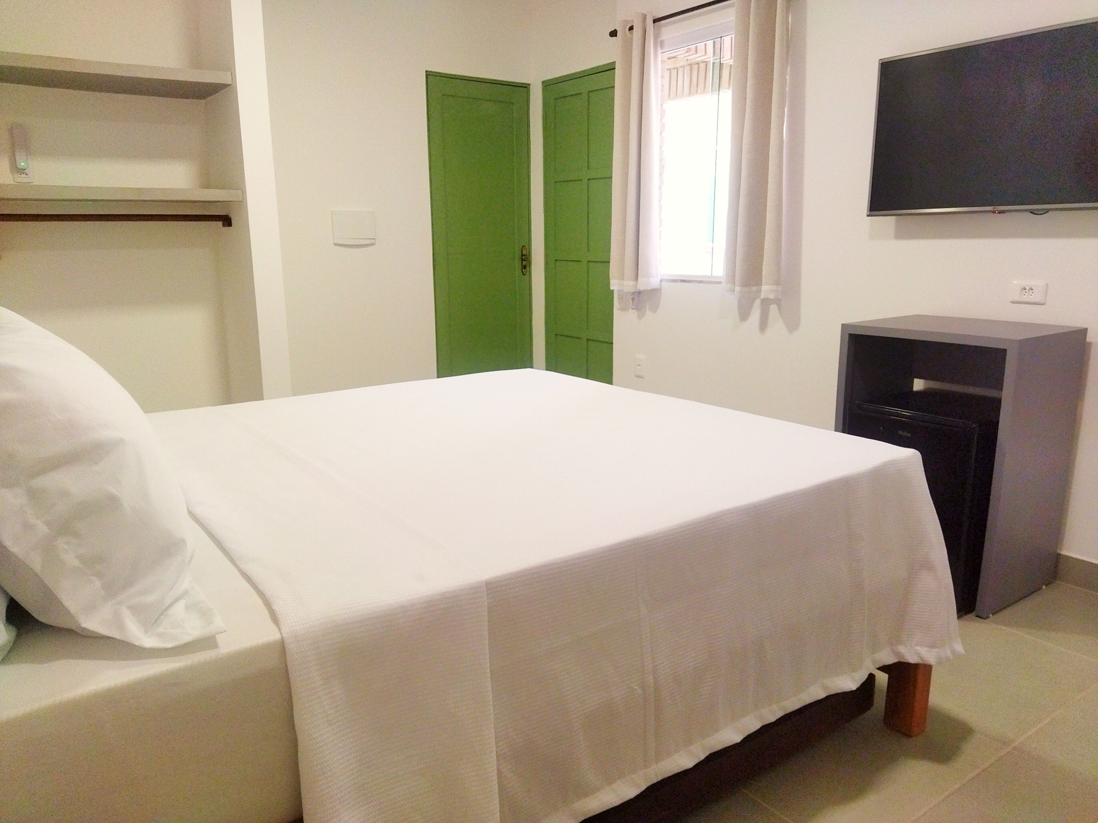 A room with a bed, a television, a green door, and a small cabinet.
