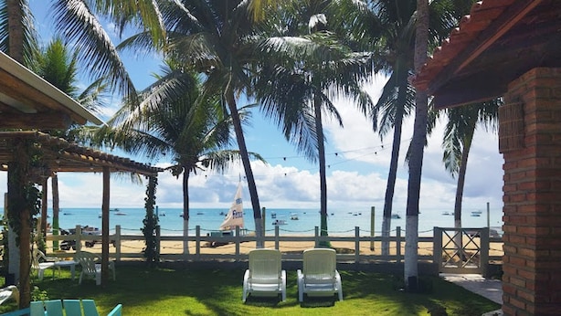 Vista sulla spiaggia con palme, un padiglione e due sedie rivolte verso l'oceano.
