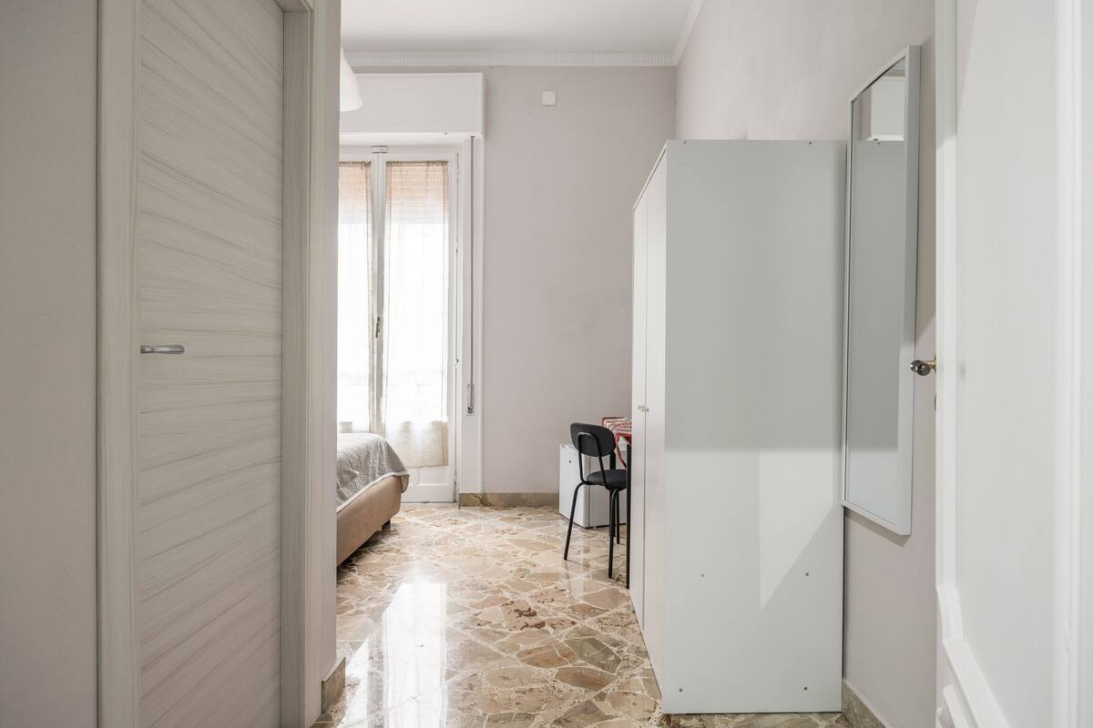 Un pasillo estrecho con una cama, un escritorio y un refrigerador.