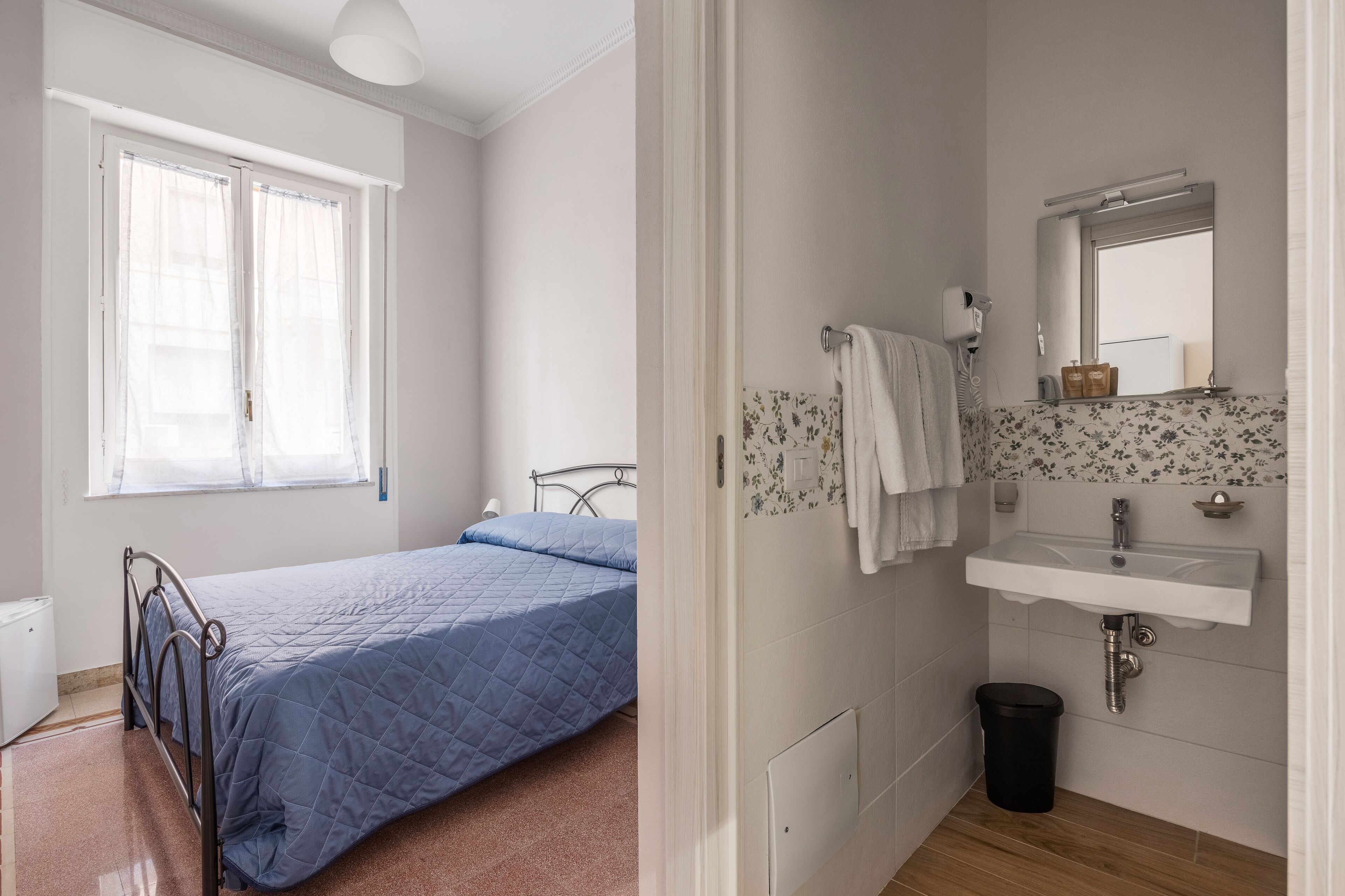 A bedroom with a bed, a window, a bedside table, and a small bedside lamp.