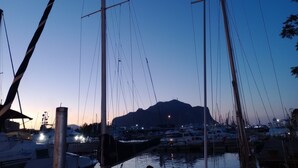 Un port de plaisance où sont amarrés de nombreux bateaux, un ciel dégagé et une montagne en arrière-plan.