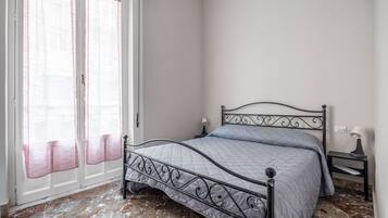 Une chambre à coucher avec un lit, une table de chevet, une lampe et une fenêtre avec des rideaux.