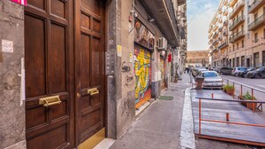 Une rue étroite, bordée de voitures garées, et un bâtiment doté de grandes portes en bois et orné d’une fresque colorée.