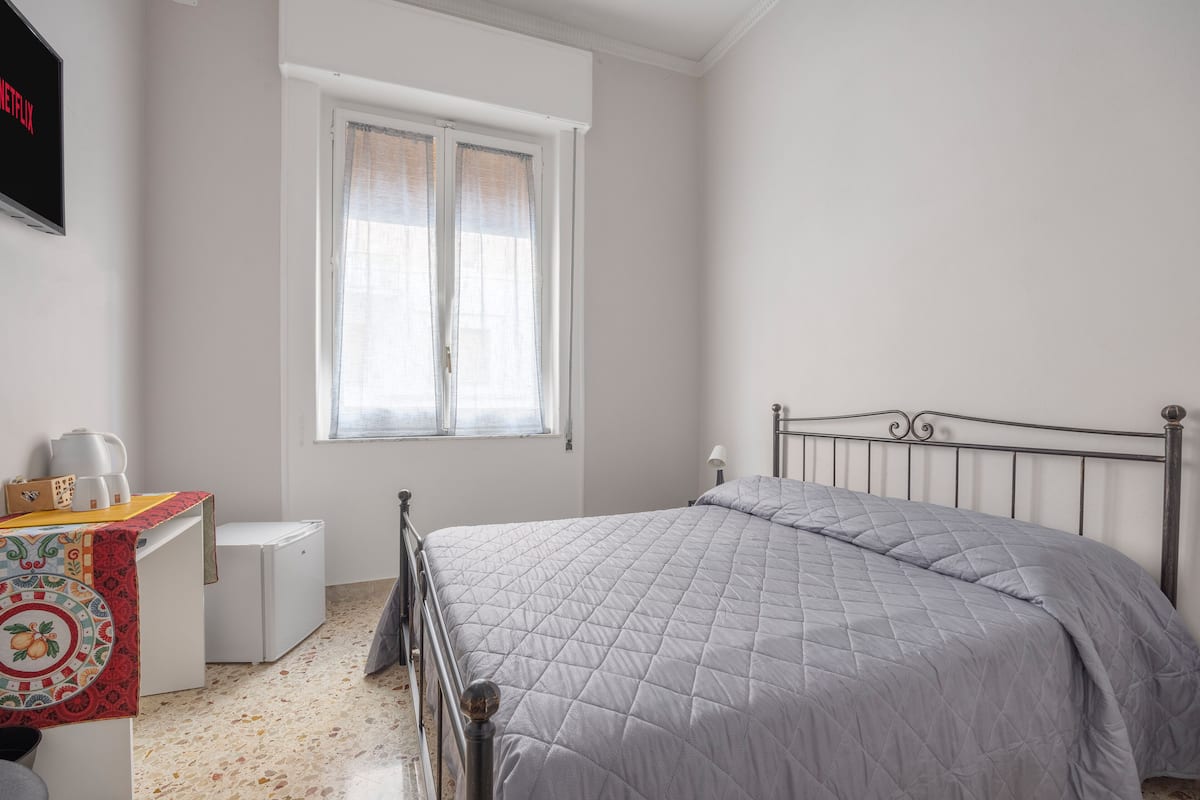 Un dormitorio con cama, un escritorio pequeño, una ventana y un televisor instalado en la pared.