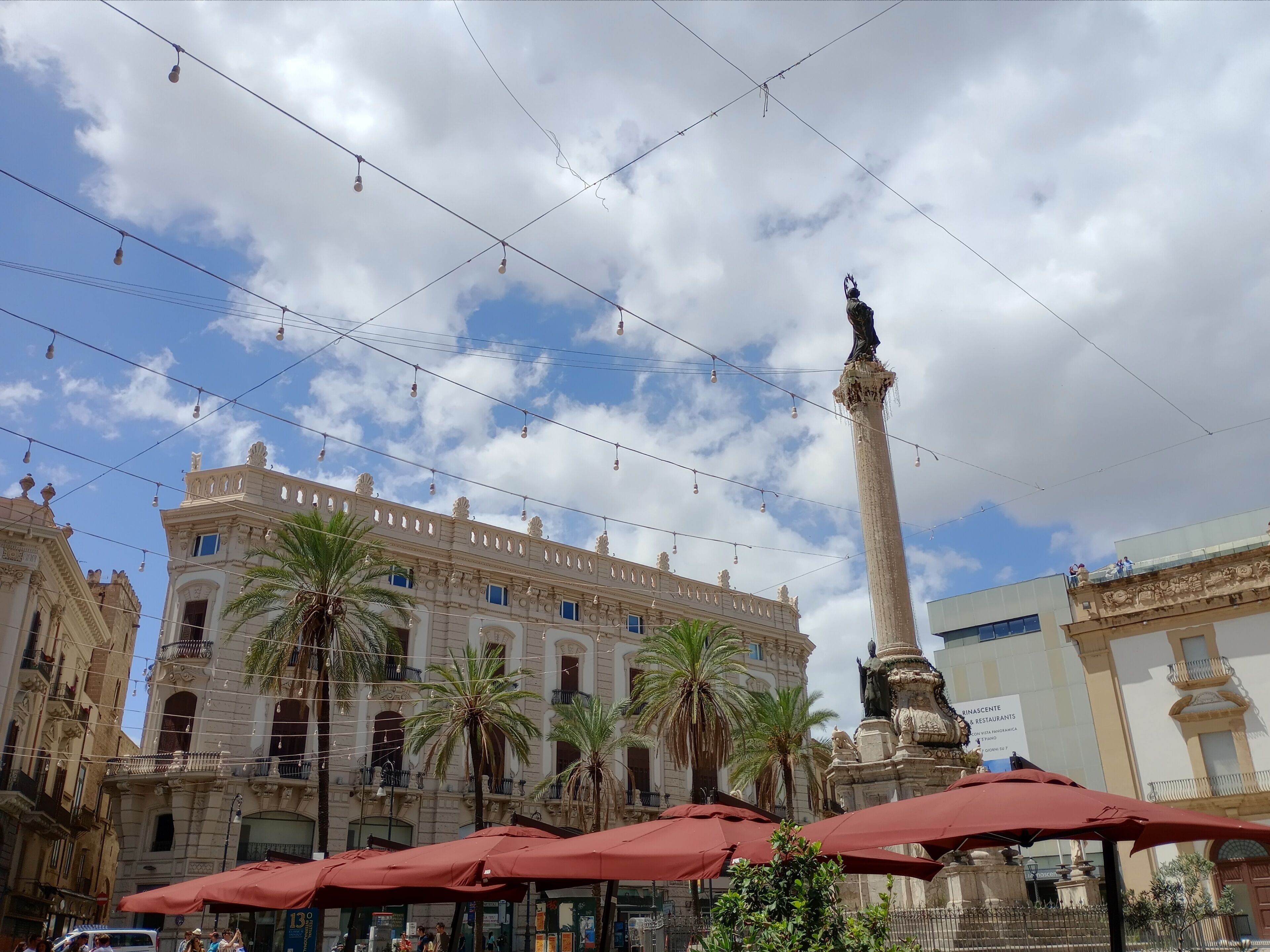 A historic building with ornate architecture, palm trees, and a tall monument.