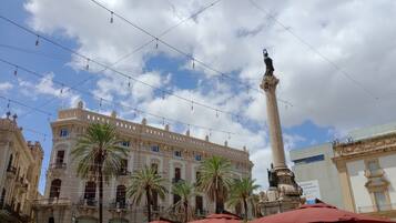 A historic building with ornate architecture, palm trees, and a tall monument.
