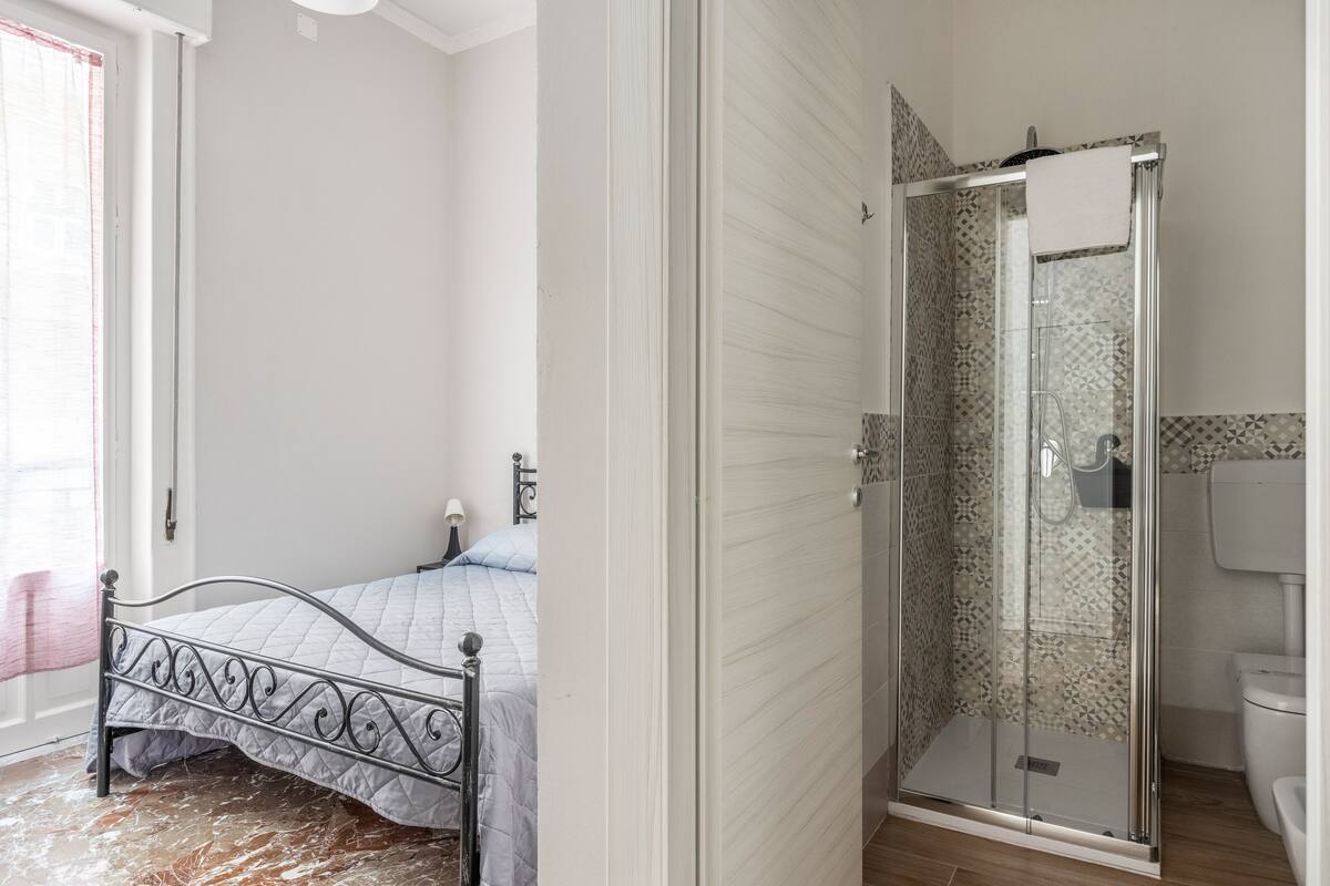 Un dormitorio con cama, ducha con puerta de vidrio y retrete.